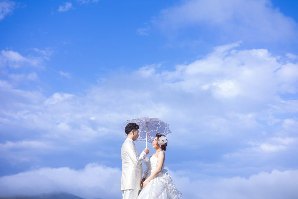 青空と日傘をさしている新郎新婦